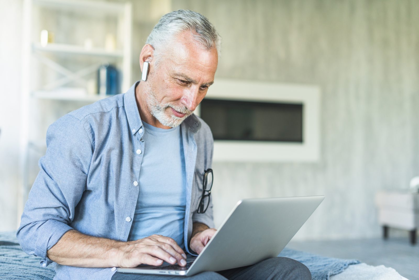 senior-man-with-wireless-bluetooth-sitting-on-bed-using-laptop.jpg